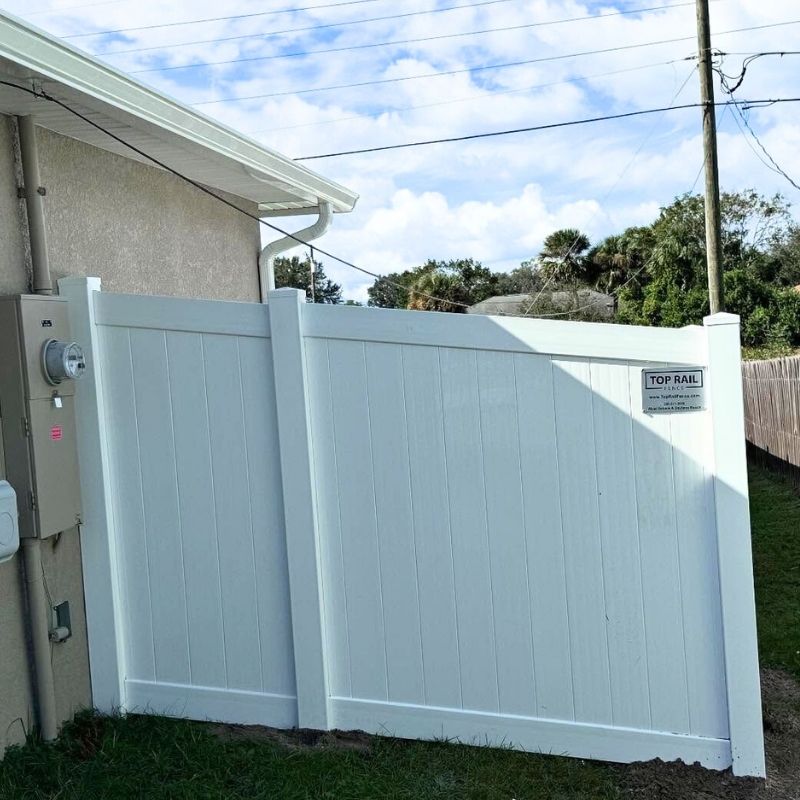 white vinyl fence attached to a house with a Top Rail Fence sign